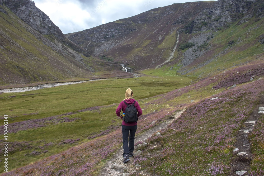 Female hiker walks in the mountains. Falls of Unich, Angus, Scotland south of the Grampian Mountains. 