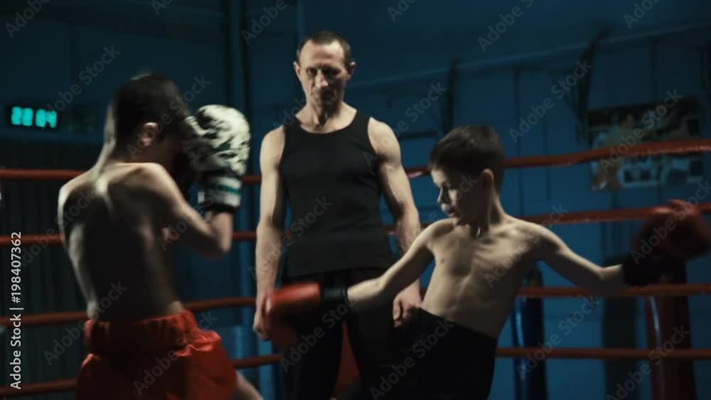Serious coach watching boys in gloves boxing and practicing Thai box in gym training together. Serious coach watching boys in gloves boxing and practicing Thai box in gym training together.