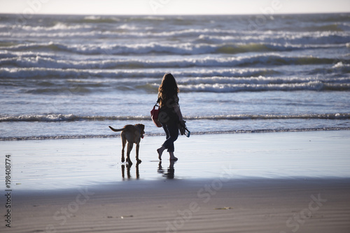 Women walking with dog on the water line of the beach on Pacific ocean with breeze and waves in Northwest
