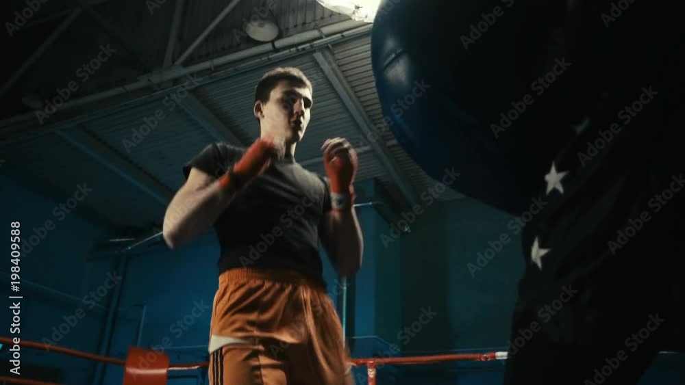 From below view of sportive athlete punching bag while working out with coach and practicing box.