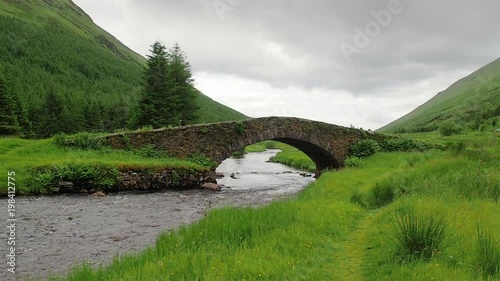 View of the stone bridge called Butterbridge in the Highlands of Scotland. Old arch bridge crossing Kinglas Water near Loch Lomond National Park. Mountain river flows through the green valley. photo