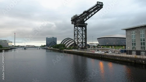 Evening view of modern buildings on the both banks of Clyde River in Glasgow, Scotland. Dramatic clouds moving over the historic Finnieston Giant Cantilever Crane and other structures. photo