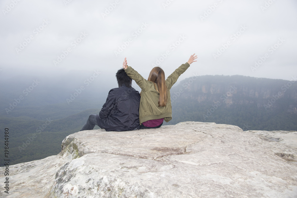Happy young couple sitting overlooking view arms out