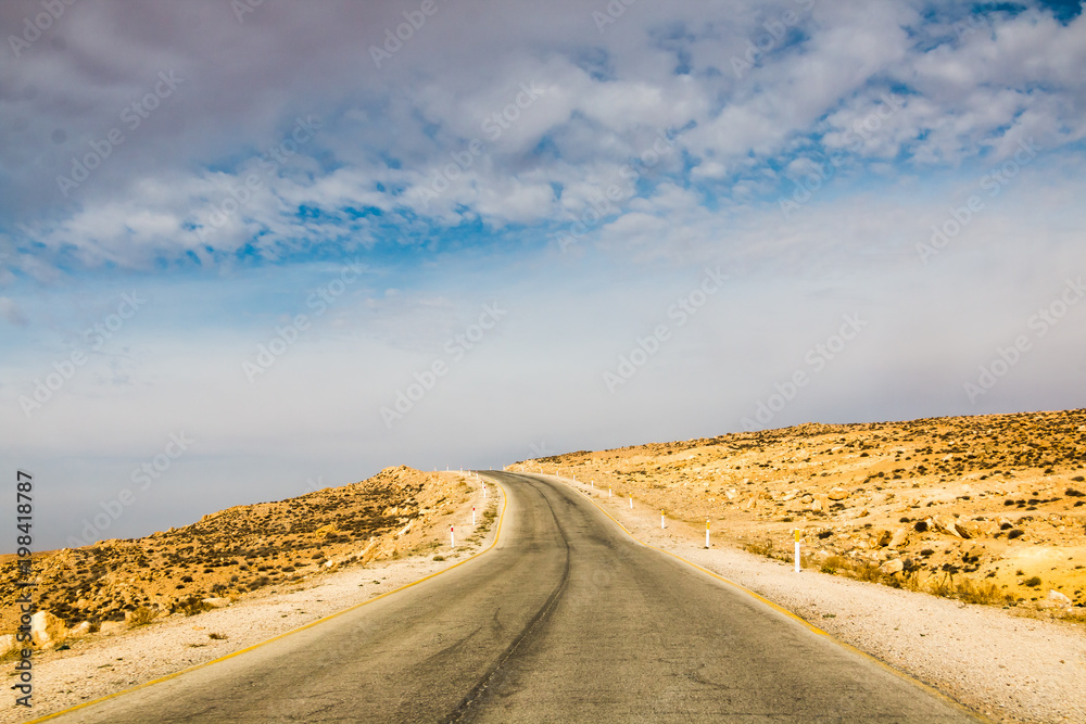 Naklejka premium The road in the desert with yellow sand and clouds on the sky