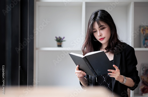 Beautiful woman in black suit sitting and reading a book in white room