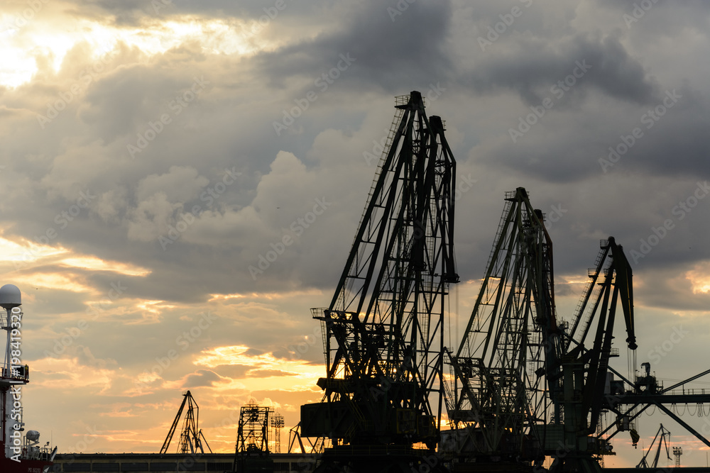 Silhouette of port cranes against a dramatic sky at sunset. Silhouette of port cranes against a dramatic sky at sunset.