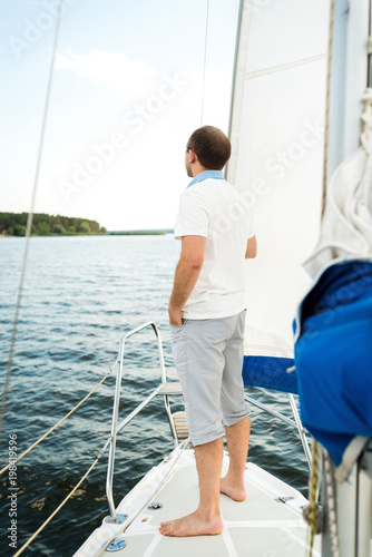 Handsome young man standing alone on yacht or sailboat in sea, copy space. Sailing, tourism, travel and people concept © mirage_studio