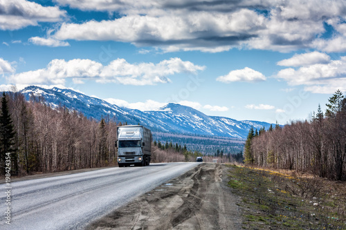 A long-distance truck with a semitrailer moves on the road among the mountains covered with snow