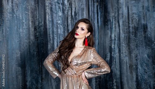 Model girl in a golden dress with a fashionable hairstyle . Portrait of a young woman whith Bright smokey eyes make up, red full lips, healthy wavy hairs