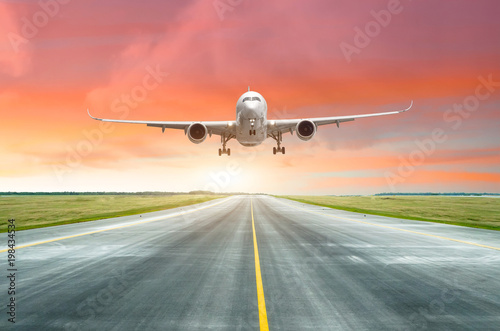 Passenger airplane landing on a runway in the evening during a bright red sunset.