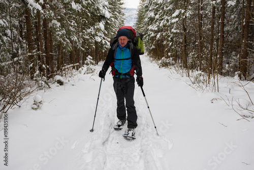 Hiker, with big backpack, is walking in snowshoes