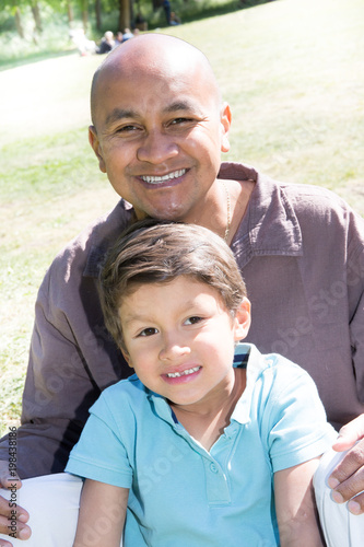 indian or mexican man sit on grass with mixed son boy child in summer