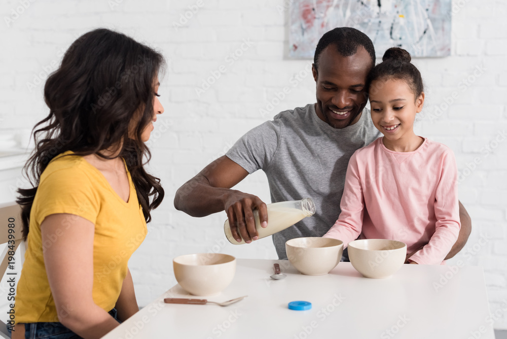 beautiful young family pouring milk into cereal breakfast beautiful young family pouring milk into cereal breakfast