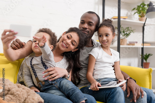 happy young family taking selfie on couch at living room