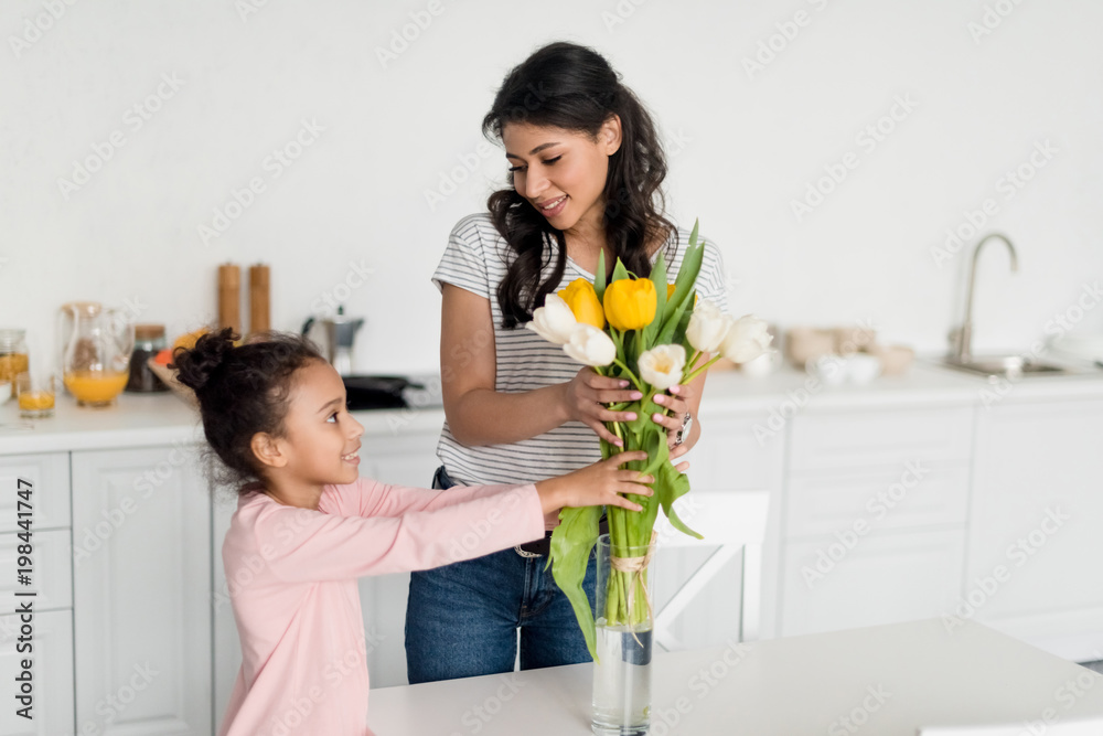 happy mother and daughter putting flowers into vase