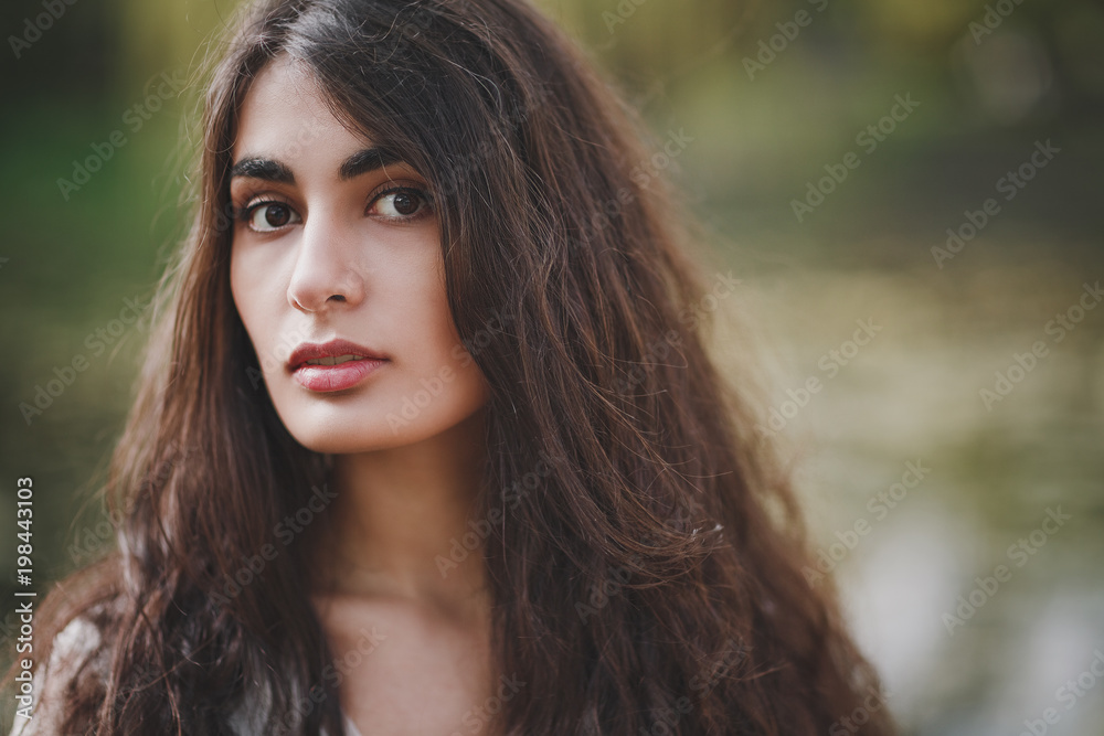 Lovely brooding brunette girl with long hair in white romantic dress stands on a wooden bridge in spring forest or park. The atmosphere of a warm sunny evening. The background is blurred. Lovely brooding brunette girl with long hair in white romantic dress stands on a wooden bridge in spring forest or park. The atmosphere of a warm sunny evening. The background is blurred.