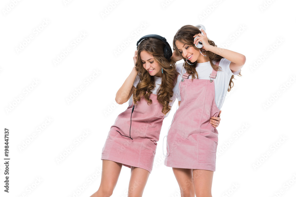 Fototapeta premium smiling young twins listening music with headphones isolated on white