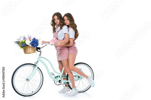 attractive young twins with bicycle and basket with flowers on white