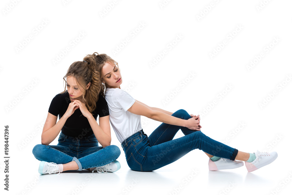 attractive young twins in jeans and shirts sitting on floor on white attractive young twins in jeans and shirts sitting on floor on white