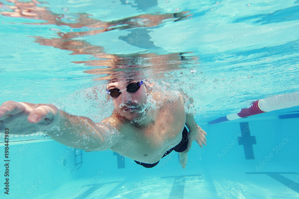 A professional swimmer trains with effort and dedication to win the race by swimming in a freestyle pool. Concept of: sport, swimming pool, competition, fitness.