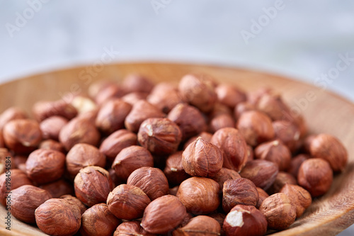 Hazelnuts in wooden plate on wihite background with copy space, top view, selective focus.