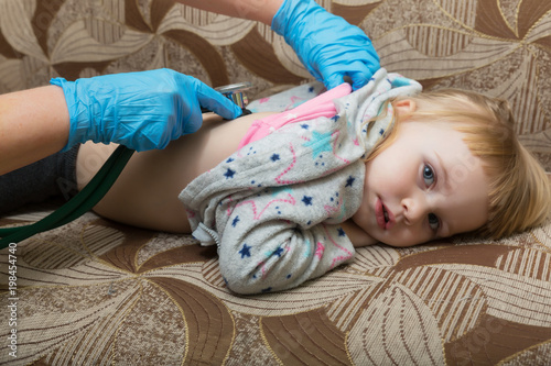 A pediatrician doctor examines the back of a sick girl using a phonostage. Home visit. photo