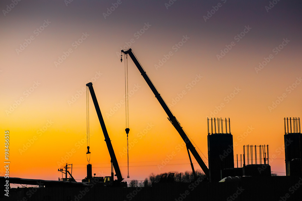 Crane and building construction site on background of sunset sky. Industrial landscape with silhouettes of cranes and building, oil and gas plant in sunlight. space for text