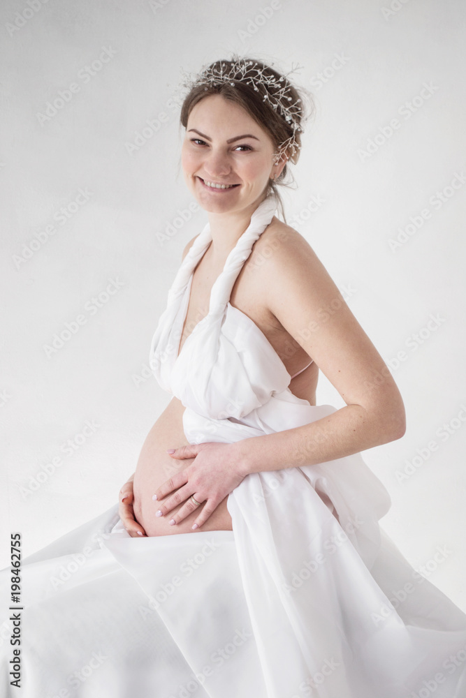 photo Pregnant girl smiling in white clothes on white background hands on stomach photo Pregnant girl smiling in white clothes on white background hands on stomach