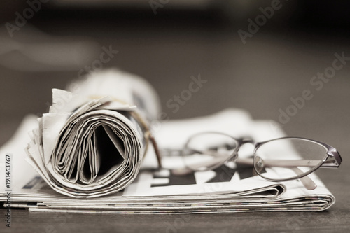 Newspapers and glasses. Folded papers with news on the desk. Headlines showen on front page, selective focus photo