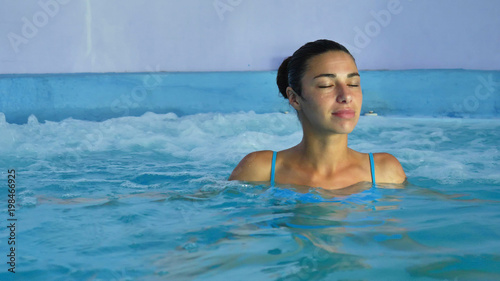 Beautiful young girl (woman) relaxed in a spa, in a blue bathing suit, on a blue background. Concept: spa procedures, body massages, spa cream, relax, spa water treatments, swimming pool