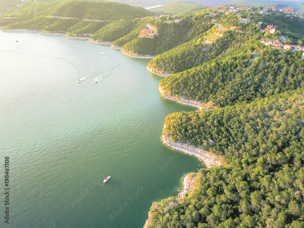 Fototapeta premium Aerial trees and cliff rock wall, bluffs at Lake Travis, Austin, Texas, USA. Luxury vacation homes and house on coastline. Looking down houses in community, ocean crystal background