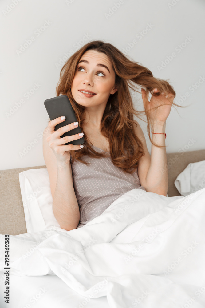 Portrait of young cute woman resting in bed after sleep with white clean linen at bedroom, and dreaming while using smartphone Portrait of young cute woman resting in bed after sleep with white clean linen at bedroom, and dreaming while using smartphone