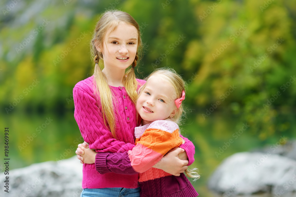 Two adorable little sisters laughing and hugging on warm and sunny summer day near Konigssee lake, Germany Two adorable little sisters laughing and hugging on warm and sunny summer day near Konigssee lake, Germany