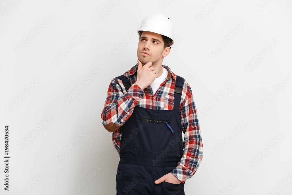 Pensive male builder in protective helmet holding his chin Pensive male builder in protective helmet holding his chin