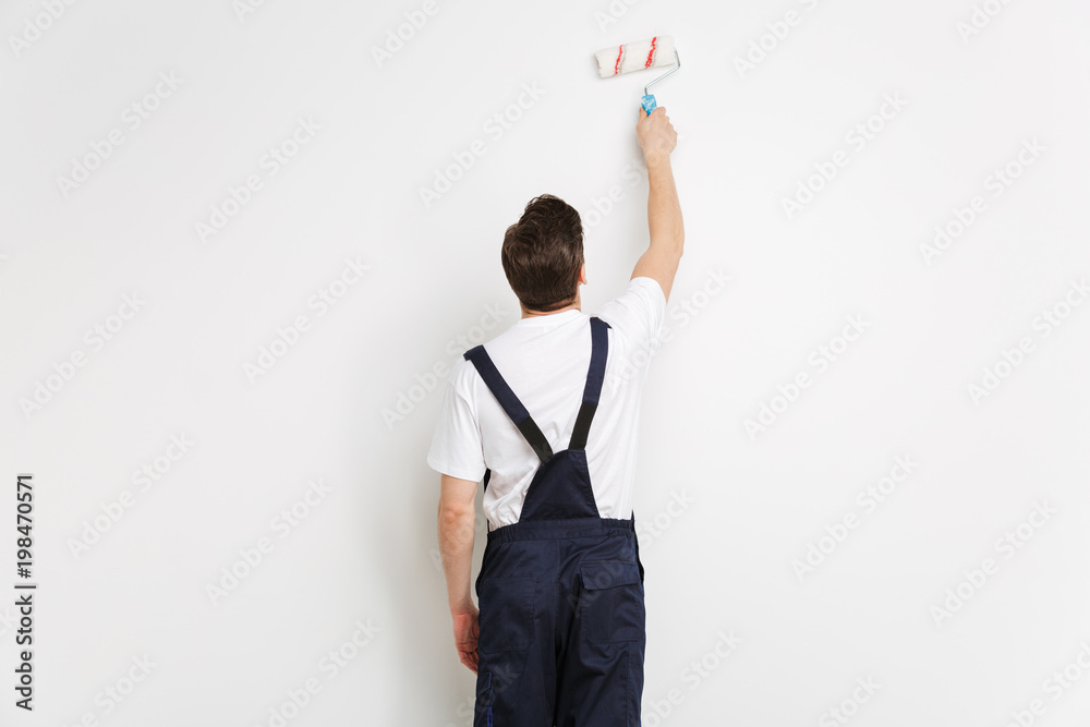 Back view of Young builder painting wall with paint roll Back view of Young builder painting wall with paint roll
