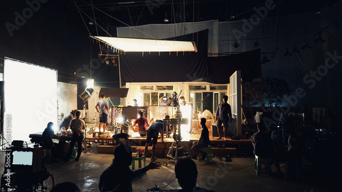 Silhouette group of people working in big production studio for shooting or filming TV commercial with highly quality digital video camera and professional lighting set and prop.