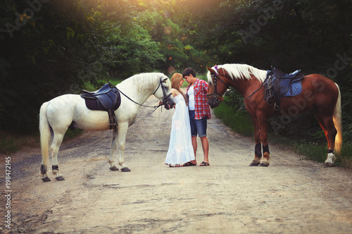 beautiful loving couple with horses stand in the woods on the road, cozy and warm artistic image, flying bright day