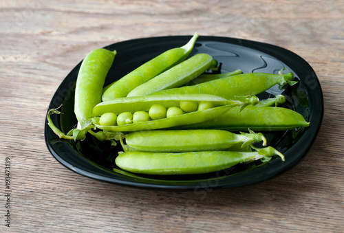 Fresh green peas in black bowl on wooden background.