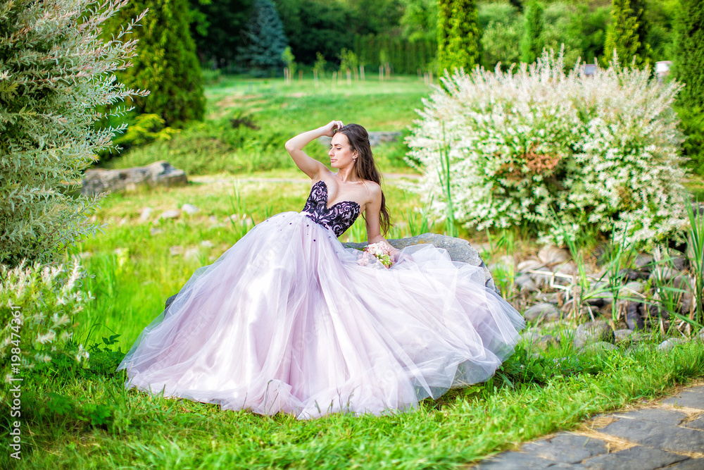 Beautiful bride in pink dress is sitting on rock in park Beautiful bride in pink dress is sitting on rock in park