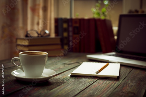 A cup of coffee in the workplace on a wooden table. A cup of coffee in the workplace on a wooden table. The concept of working outside the office