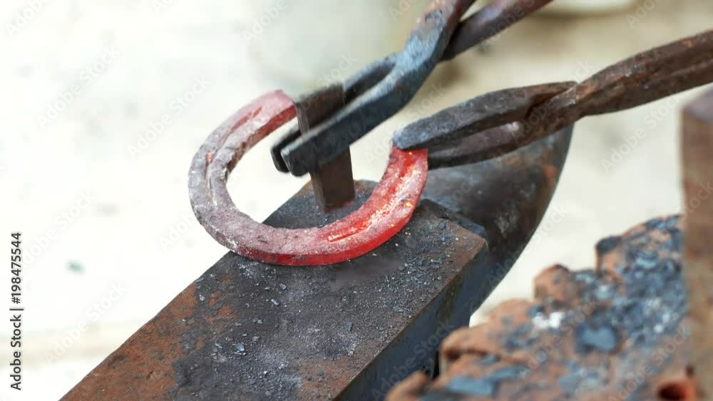 A blacksmith pounding a hammer on red-hot horseshoe on the anvil.