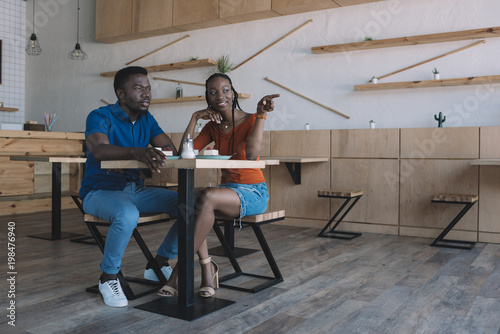 smiling african american couple sitting at table with cups of coffee and desserts in cafe