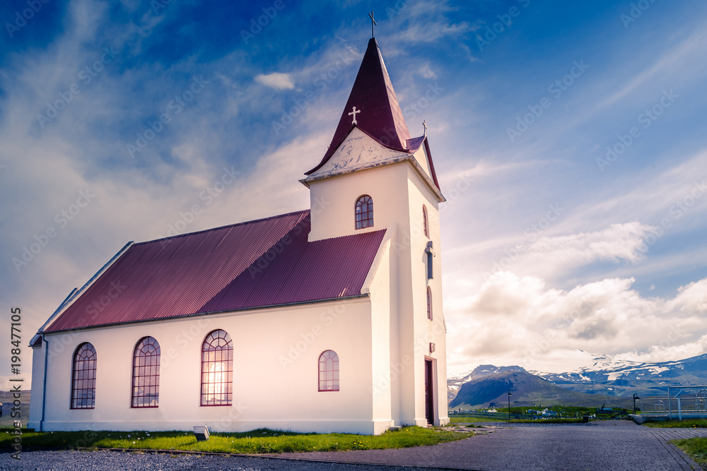 Ingjaldsholskirkja local lutheran church in sunset lights, with mountains and glaciers  in the background, Hellissandur, Iceland