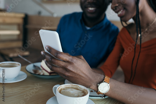 cropped shot of african american couple using smartphone together in cafe