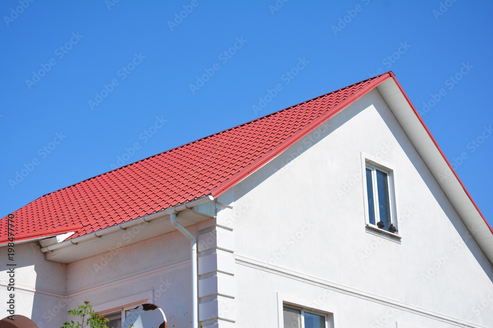 House with plaster walls, attic window, red metal roof and white
