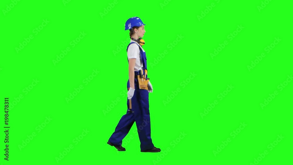 Worker girl comes with a hammer in her hands and in a helmet. Green screen. Side view