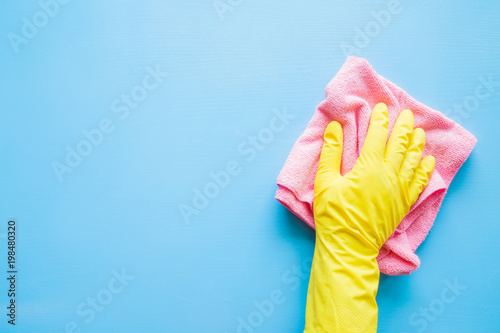 Employee hand in rubber protective glove with microfiber rag wiping blue table, wall or floor surface in room, bathroom, kitchen. Early spring or regular cleanup. Commercial cleaning company concept.