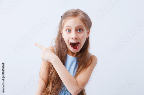 Obraz na plátně Surprised astonished child has shocked expression, points with fore finger at copy space on  background