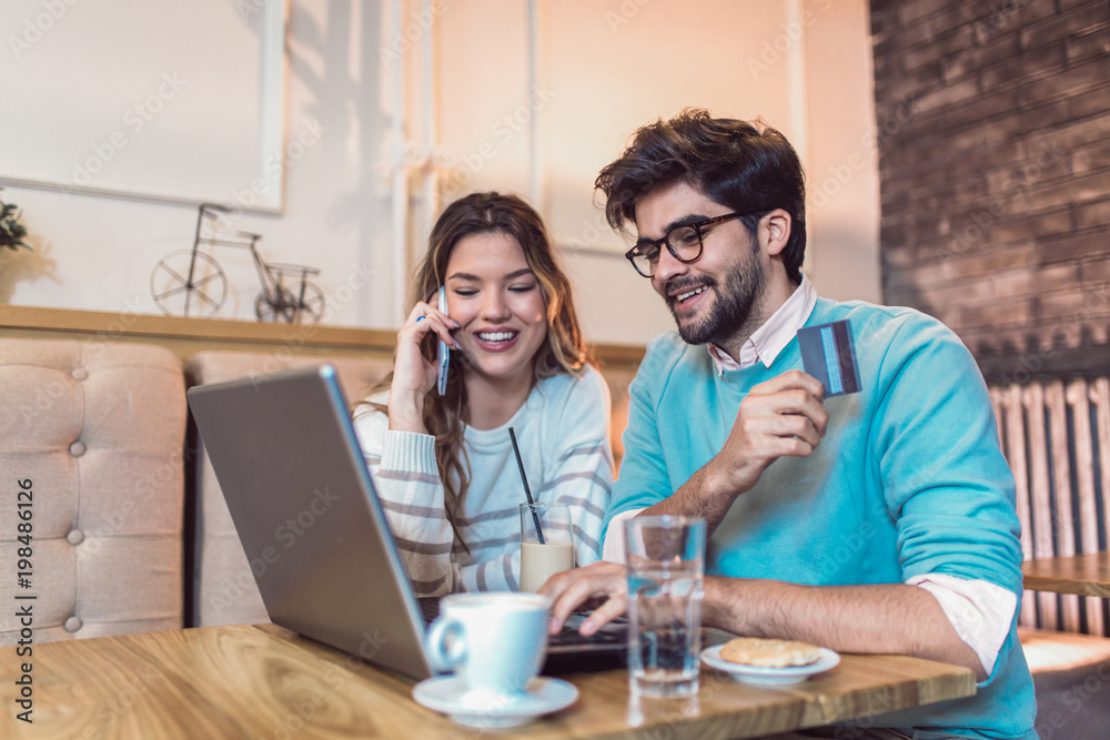 Happy young couple sitting at cafe and shopping online. Woman holding credit card. Happy young couple sitting at cafe and shopping online. Woman holding credit card.