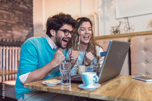 Happy young couple sitting at cafe and shopping online. Woman holding credit card.